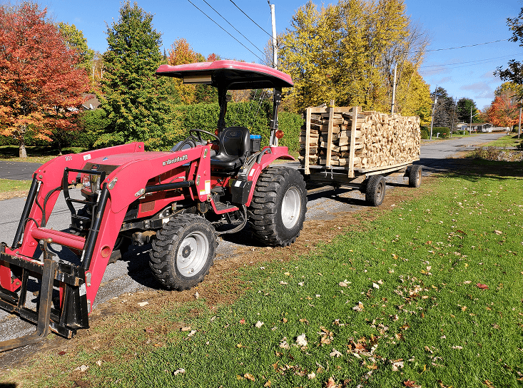 A tractor pull a cart of chopped wood.